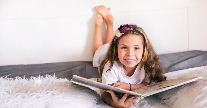 Schoolgirl reading a book in the room. Girl 8 or 10 years old with a book in the room on the bed. A child in a bright interior to study at home. Copy space. Banner. High quality photo