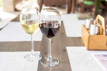 a glass of fragrant white and a glass of ruby red wine on a wooden table in a restaurant, selective focusing, dry white wine in a glass and semi-sweet red, expensive wine