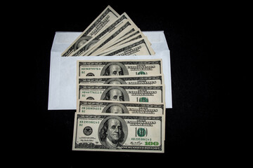 One hundred dollar bills in a white envelope on a black background. Bribery concept. Salary in...