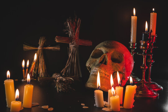 Old Skull and candle with incense on old altar plate which has dim light. Select focus, black background. Straw voodoo dolls.