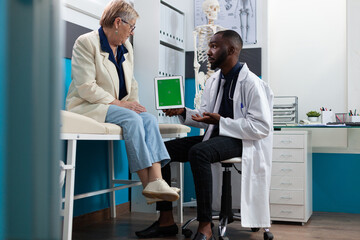 Specialist doctor man holding mock up green screen chroma key tablet computer with isolated display explaining sickness diagnosis discussing healthcare treatment in hospital office. Medicine concept