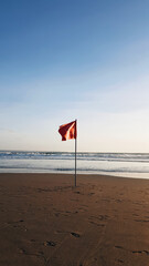 Red flag on the ocean beach. A red flag on the beach means that the sea is dangerous, high waves and swimming is prohibited. flag against the blue sea and sky. The flag will be reflected on the wet sa