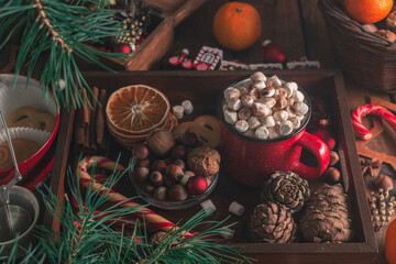 In a wooden tray there is a mug with marshmallows and New Year's attributes
