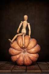 A wooden gestalt mannequin is engaged with a pumpkin on a wooden table and an art background for Halloween.