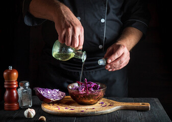 Professional cook pours olive oil into a fresh red cabbage salad. Cooking healthy food in restaurant kitchen on vintage table.