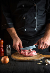 The cook cuts meat with a knife in the kitchen prepares food. Vegetables and spices on a table in a restaurant for preparing a delicious lunch