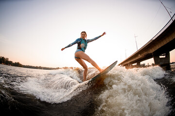 beautiful wet woman energetically balancing on great splashing wave on wakesurf.