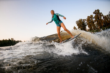 woman engaged in water sport and masterfully trying to stand on splashing wave on wakesurf