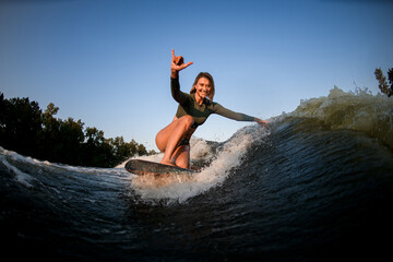 cheerful woman sits on surf rides and touches waves with one hand and show hand gesture