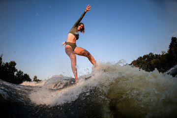 Healthy athletic woman balancing on wakesurf board on the river wave