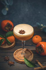 Glass of Persimmon Ginger Gin Fizz served on dark wooden table surface. Cocktail for Christmas,...