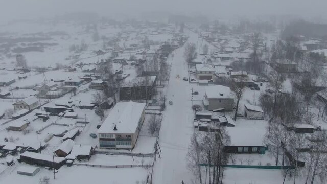 Aerial shot in back movement of snowed town when strong snow-storm. Road in center of frame