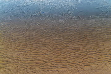 Thin ice on the water of a sand pit with a transparent sandy bottom . Leningrad region, Vsevolozhsk.