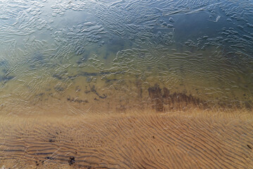 Thin ice on the water of a sand pit with a transparent sandy bottom . Leningrad region, Vsevolozhsk.