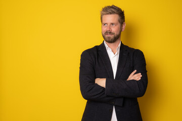 Young caucasian man wearing elegant clothing with arms folded looking side isolated over yellow background.
