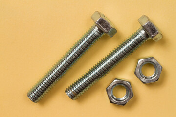 Two shiny metal bolts and two nuts on a yellow background.