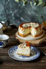 cheesecake with caramel and almonds on a white plate and a wooden board. Side view, green and wooden background.
