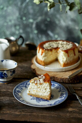 cheesecake with caramel and almonds on a white plate and a wooden board. Side view, green and wooden background.