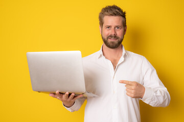 Portrait of a excited young man holding laptop computer isolated on yellow background.