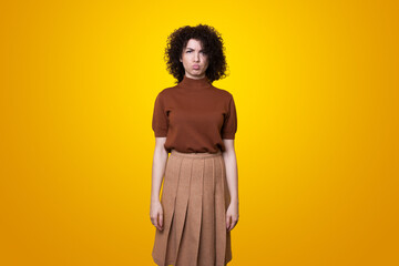 Portrait of displeased offended woman with curly hair looking angrily at camera isolated over yellow studio background.