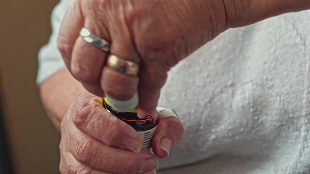 Senior woman removes the sealing ring around the plastic cap on vitamin pill bottle