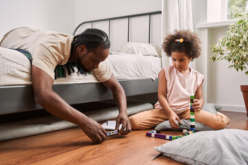 Man laying at bed and examining detail from building kit while playing with his daughter