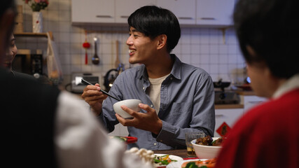 selective focus of hungry asian adult male father reaching for delicious food and burning his mouth while eating reunion dinner with family on chinese new year’s eve at home