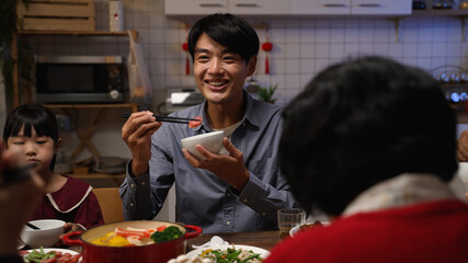selective focus smiling asian father talking to family while enjoying tasty food at dinner table. people chatting happily during reunion meal on lunar new year’s eve at home - obrazy, fototapety, plakaty