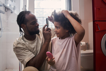 Multiracial man with dreadlocks doing hairstyle for his little daughter