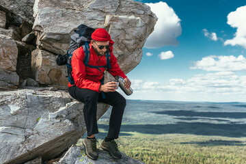 A bearded traveler with a backpack on top of a mountain. Portrait of a traveler in red clothes and...