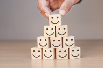 Hand holding wooden cube with smiley face icon. Customer Service Satisfaction Concept