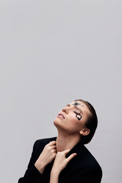 Fashion model with eyes closed touching lapels of jacket in front of white background
