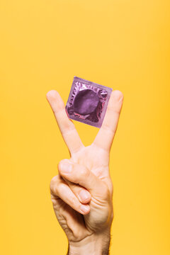 Man with condom packet gesturing against yellow background