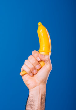 Man holding banana covered in yellow condom against blue background
