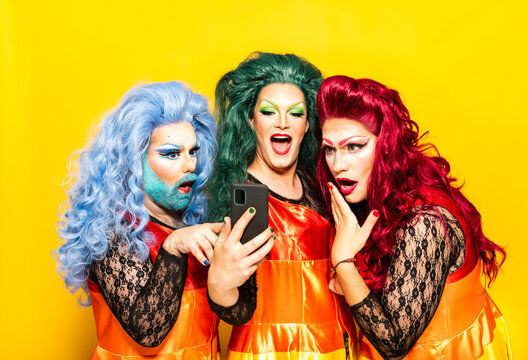 Surprised drag queens using mobile phone against yellow background