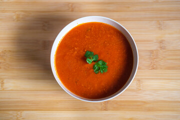 Home made tomato soup with sprig of parsley on a wooden chopping board