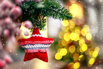 Red star christmas bauble in fir branch on blurred garland light background