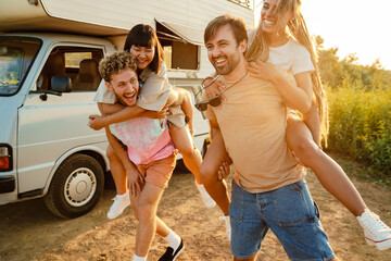 Multiracial two couples laughing and piggybacking by trailer
