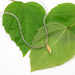 Female golden wing shaped pendant with transparent beads chain neсklace on green
