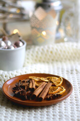 Fototapeta na wymiar Plate with cinnamon, anise and dry oranges, cozy blanket, various Christmas deocrations and lit candles. Hygge at home. Selective focus.