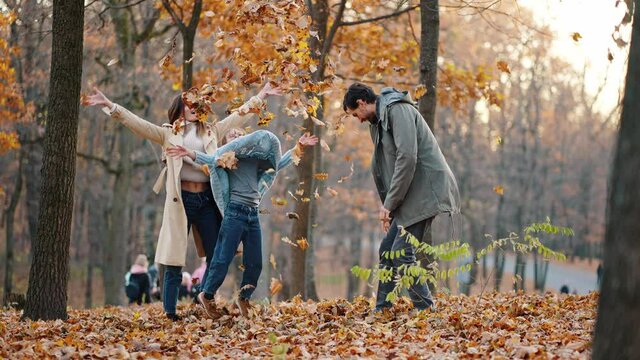 Young mother, father and little daughter laughing, fooling around and throwing up yellow foliage while playing in autumn park. Slow motion