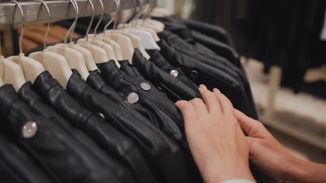 Close-up of women's hands in a clothing store choosing a leather jacket on hangers.