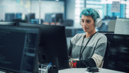 In Diverse Office: Young Stylish Woman in Headphones Working on Desktop Computer. Digital...