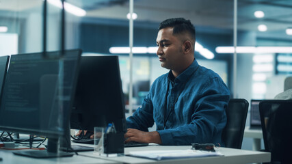 In Diverse Office: Portrait of Handsome Indian Man Working on Desktop Computer. Focused Professional Creates Innovative Software, Modern App Design. Stylish Multi-Ethnic Authentic Workplace