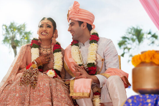 Happy Indian bride and groom sitting together at wedding mandap