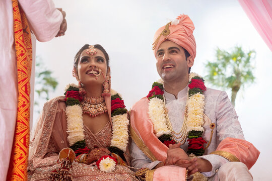 Happy Indian bride and groom sitting together at wedding mandap
