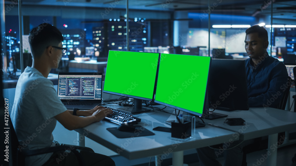 Aufkleber Night Office: Young Japanese Man in Working on Green Screen Chroma Key Desktop Computer. Team of Programmers Typing Code, Creating Modern Software, e-Commerce App Design, e-Business Programming