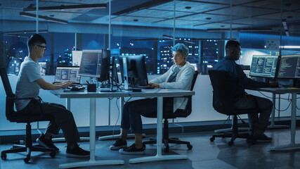 Fototapeta premium Diverse Office at Night: Multi-Ethnic Team of Young Programmers Working on Desktop Computers, Screens Show Coding Language User Interface. Software Engineers Create Innovative e-Commerce App.