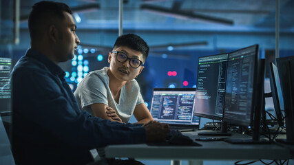 Teamwork In Diverse Office at Night: Project Manager Talks with Creative Solutions Specialist, They Discuss App Code Computer. Stylish Professionals Programming, Create e-Commerce Software