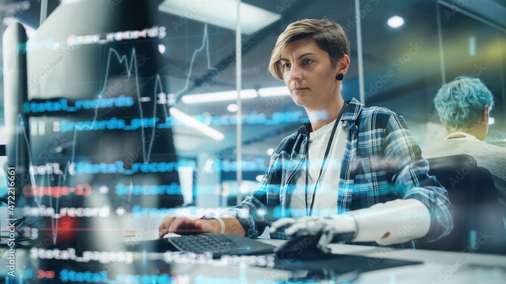 Poster Shot with Visualisation of Running Computer Code on Foreground. Portrait of Motivated Woman with Disability Using Prosthetic Arm to Work on Computer in Body Positive Office. Myoelectric Bionic Hand